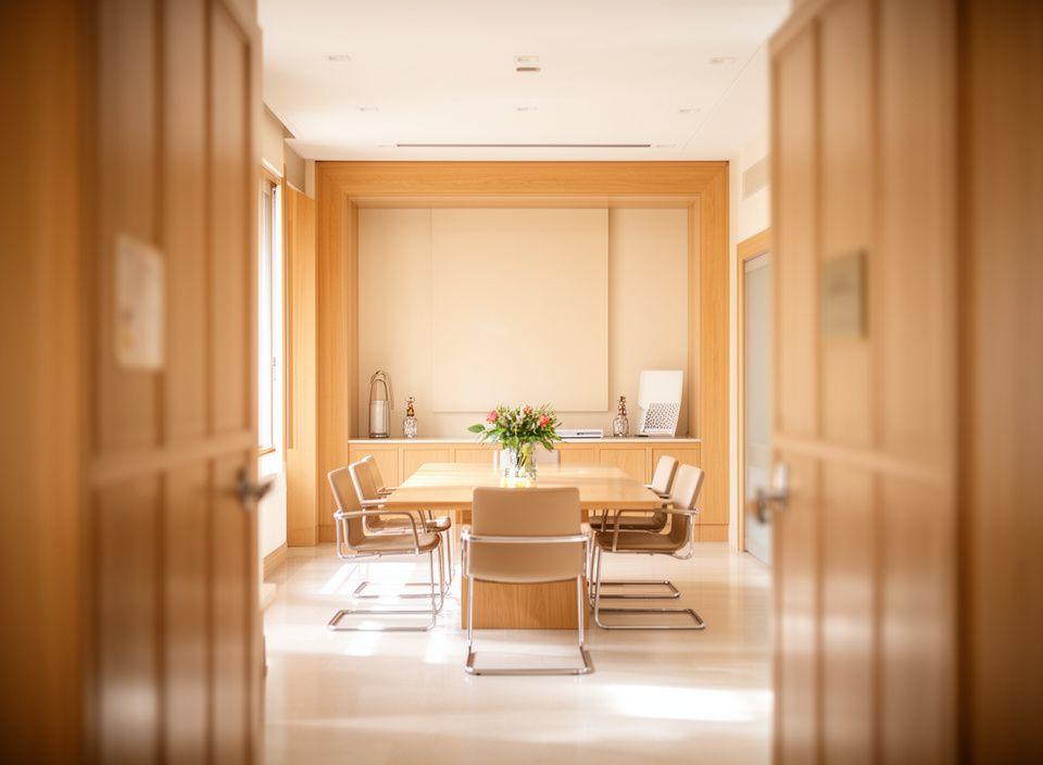 Entrada luminosa de un despacho legal en Madrid con mesa de reuniones, luz natural y detalles de madera